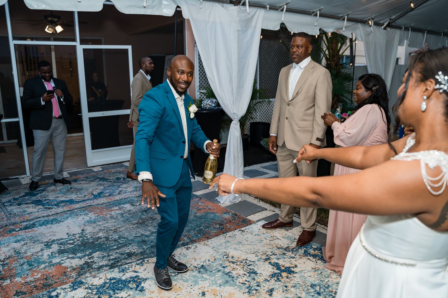 Groom in vibrant blue suit dances at outdoor wedding reception on patterned carpet.