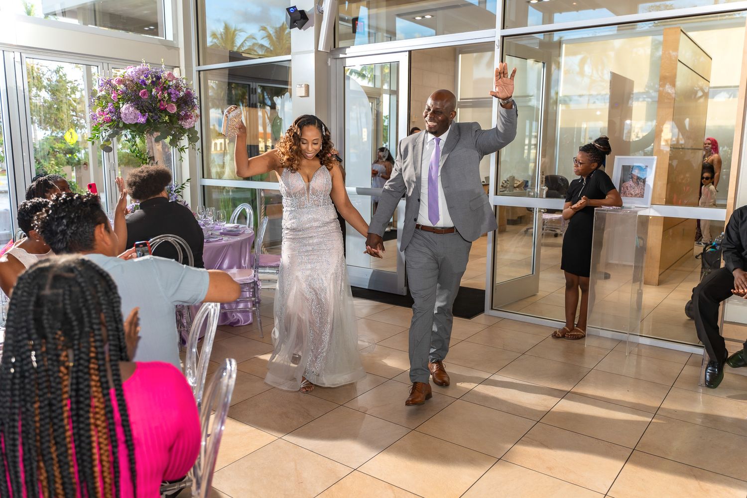 A couple makes their grand entrance at a wedding reception in a bright sunlit venue.