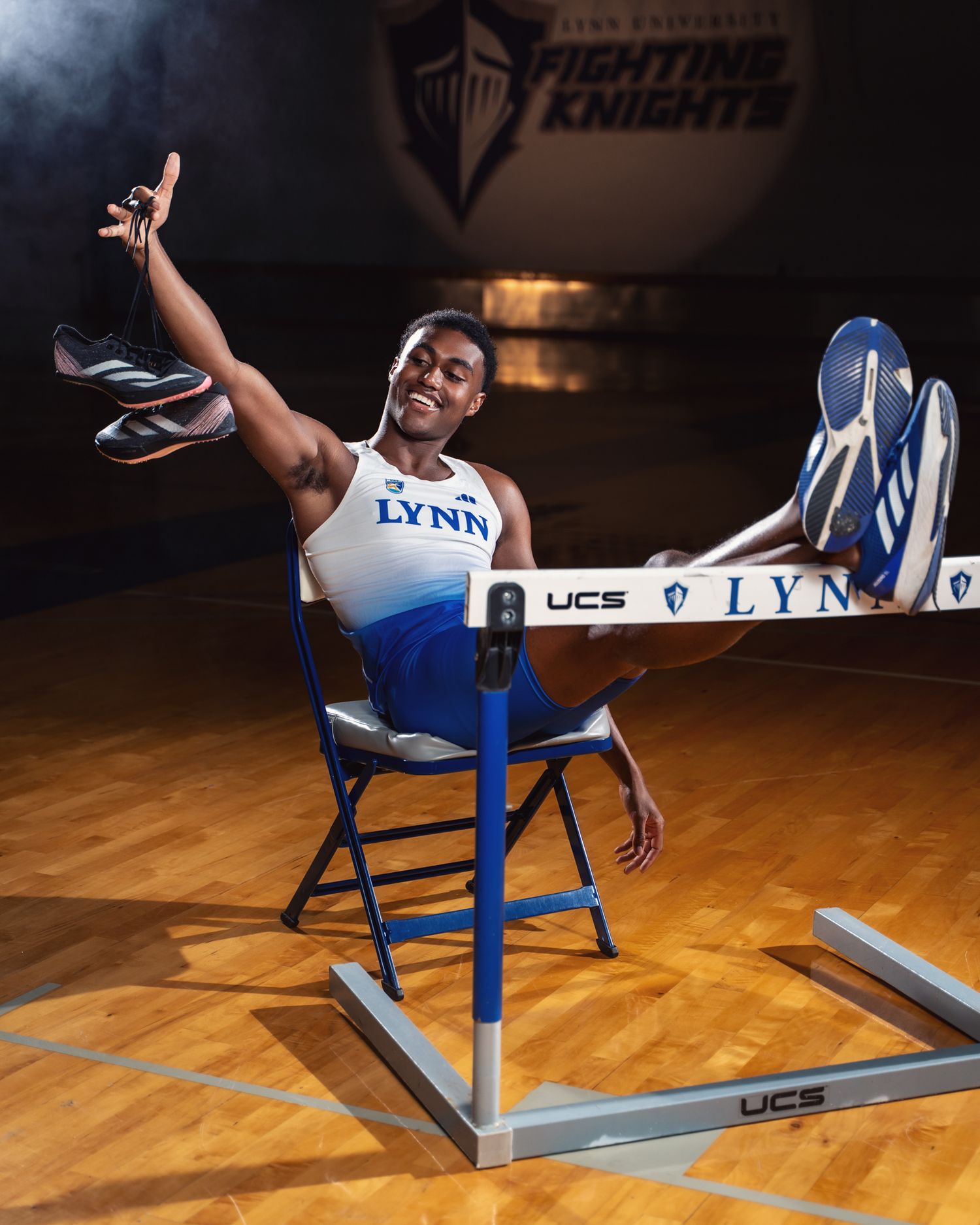 Lynn University athlete performs creative pose on chair with hurdle for sports portrait.