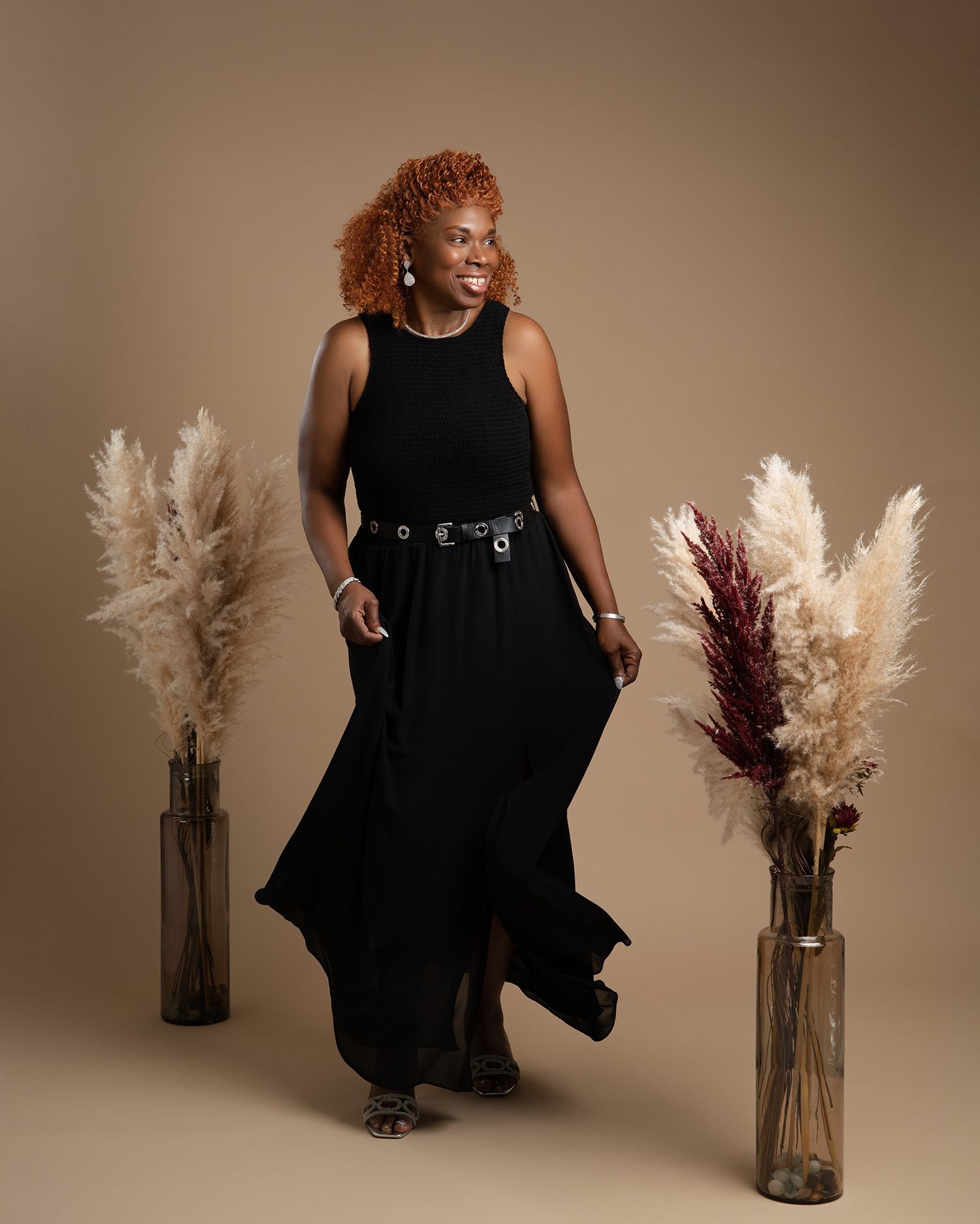 Studio portrait showing a flowing black dress and decorative pampas grass arrangements in glass vases.