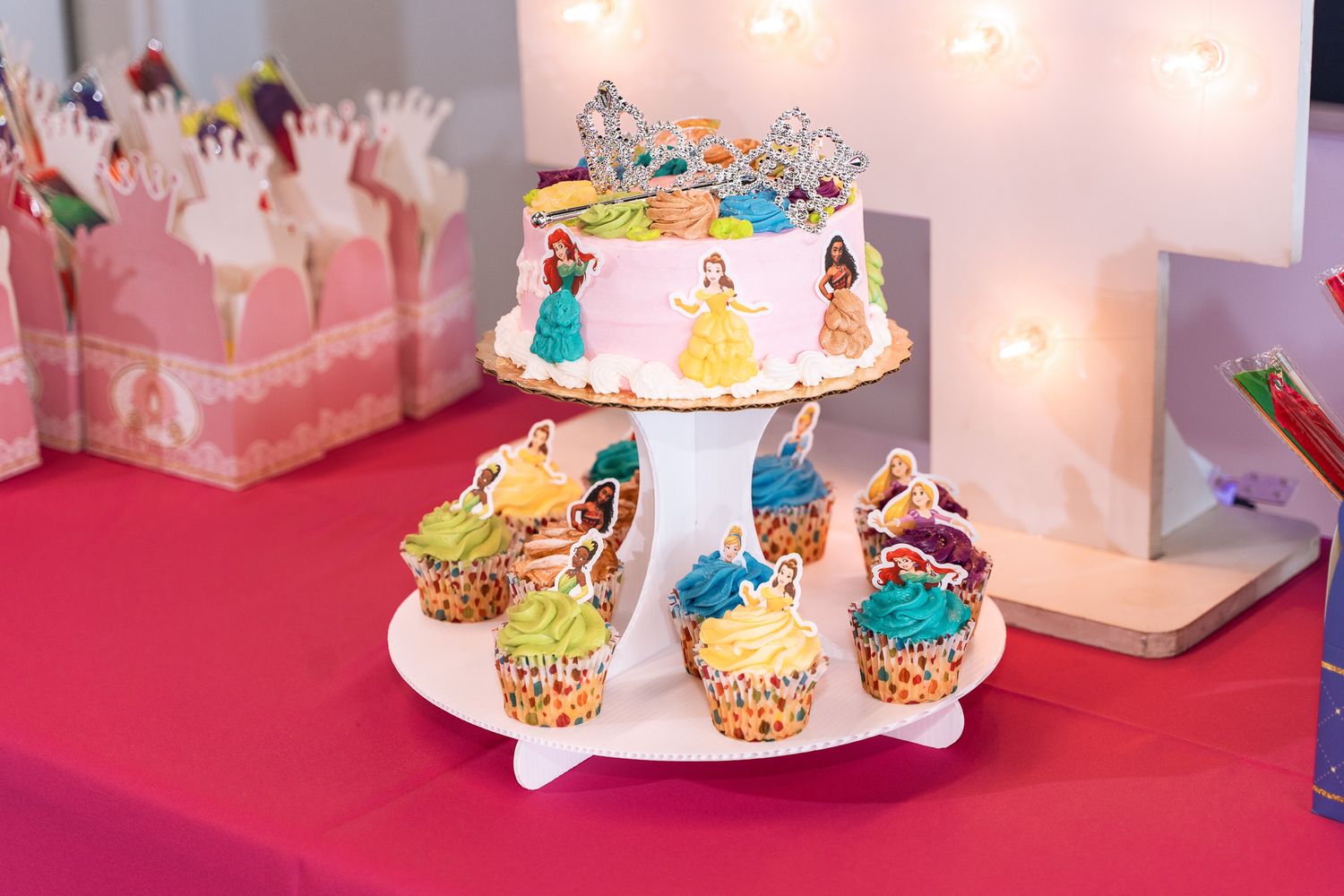 Colorful princess-themed cake and cupcakes displayed on a tiered stand at a party.