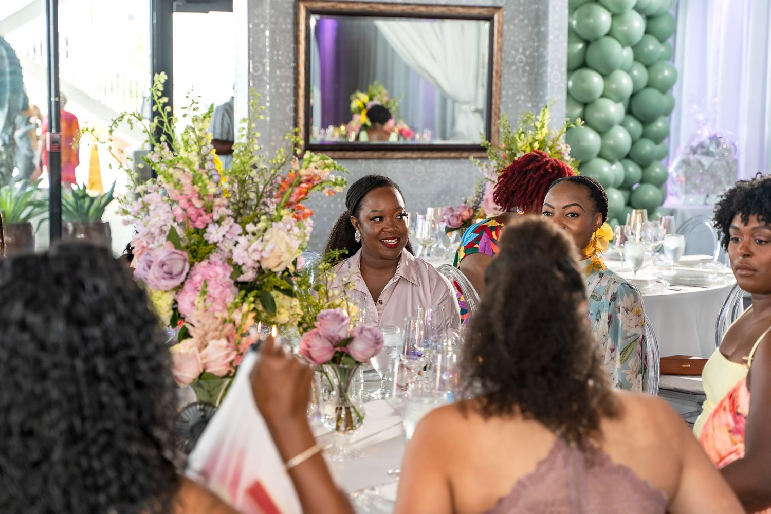 Baby shower celebration with guests gathered around elegantly decorated table with floral arrangements.