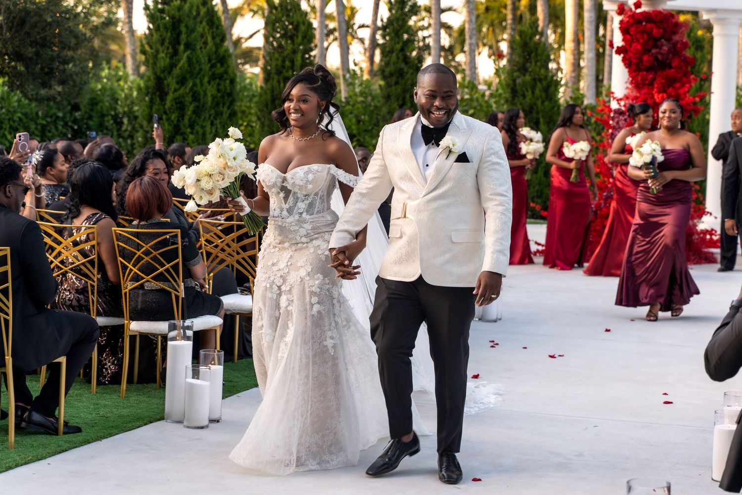 Wedding ceremony setup with white chairs and floral arrangements under palm trees at sunset.