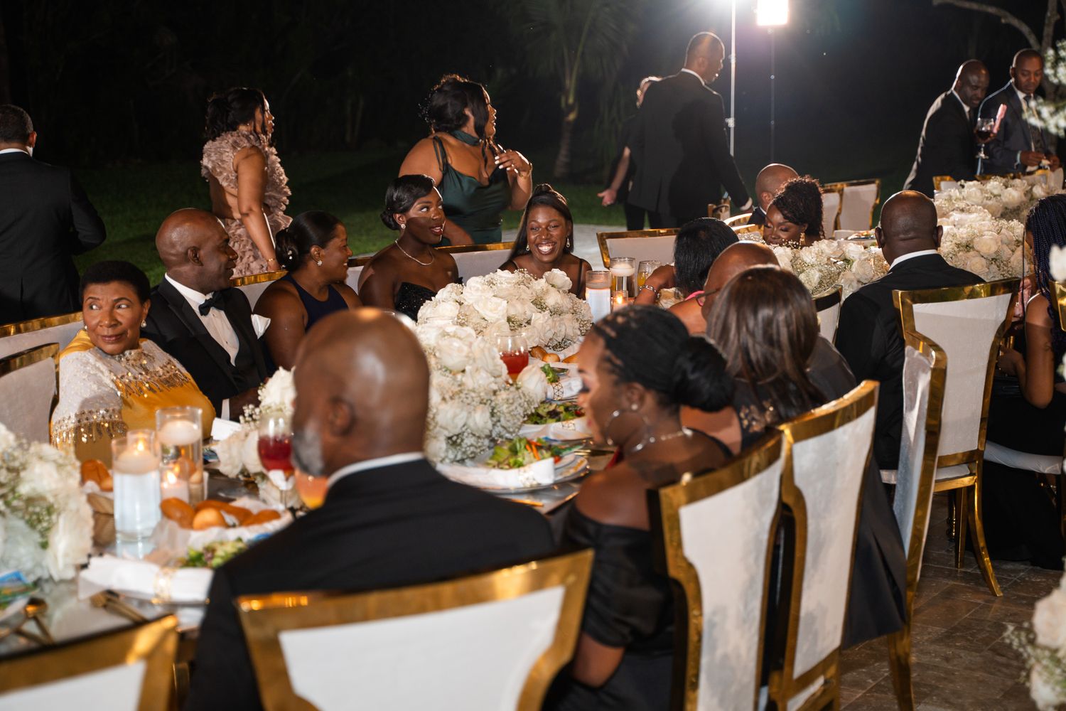 Wedding reception guests dining at an elegantly decorated table with gold chairs.