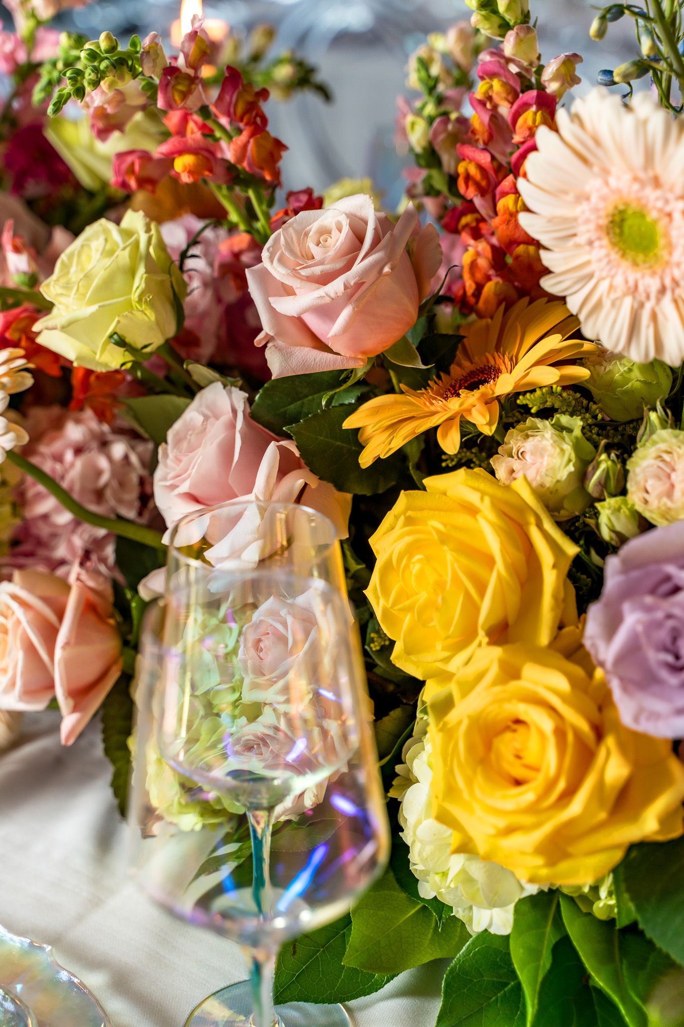 Colorful floral arrangement with roses, gerberas and greenery next to crystal glassware.