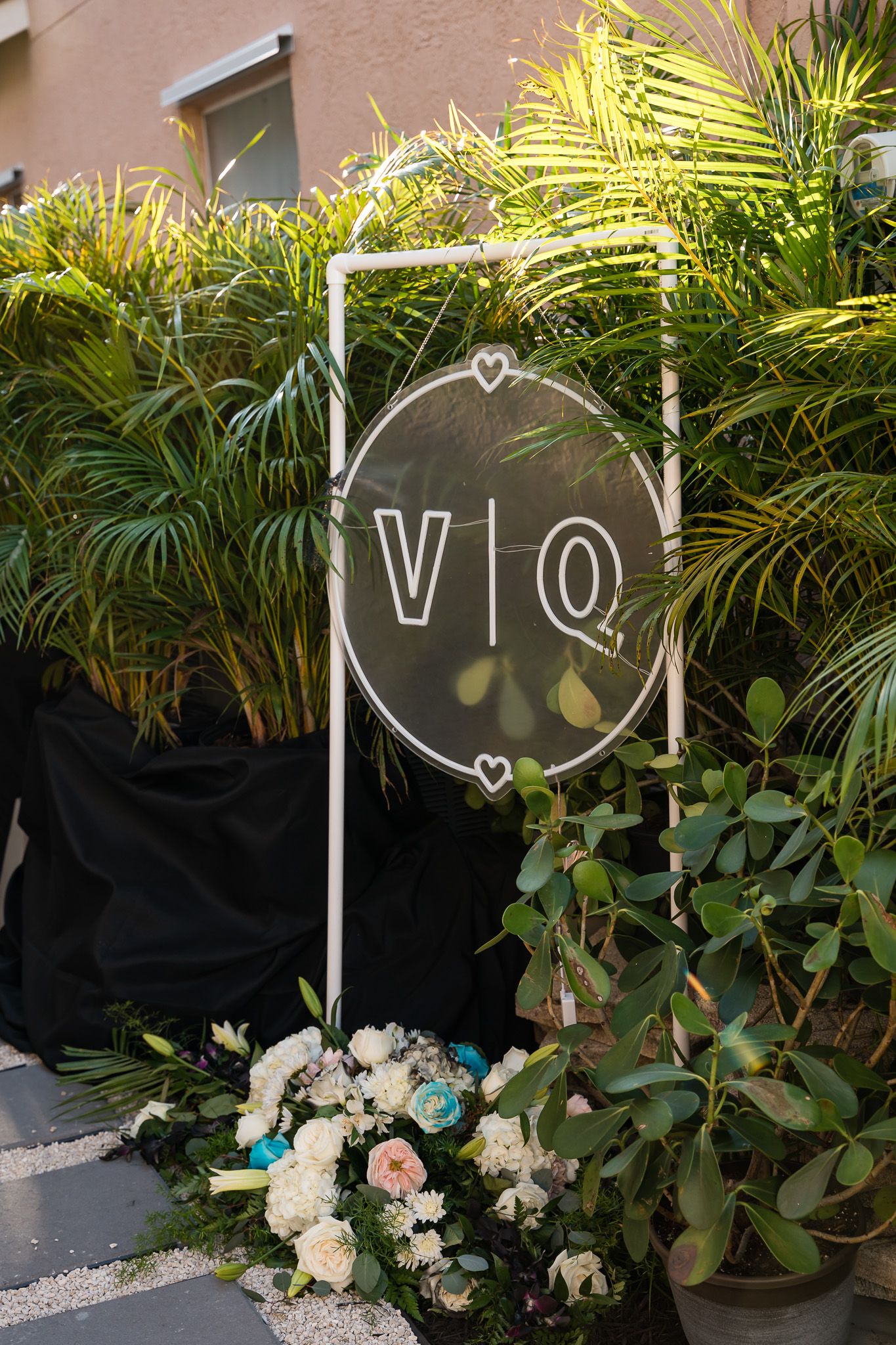 Wedding monogram sign with V Q letters surrounded by tropical plants and white flowers.