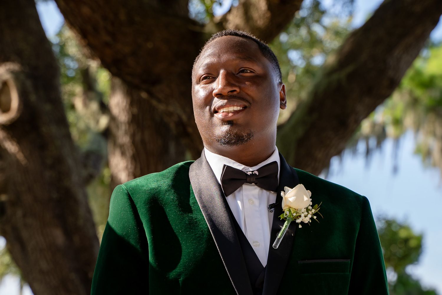 Wedding attendee in an emerald green velvet tuxedo and bowtie smiles outdoors.
