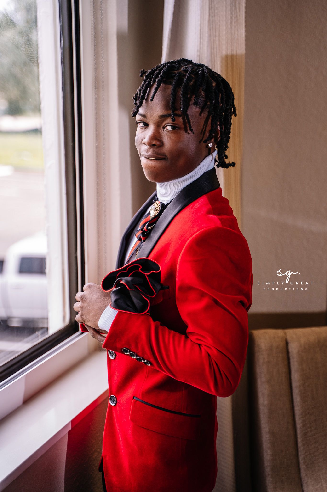 Person wearing red blazer and tie smiling while standing by window.