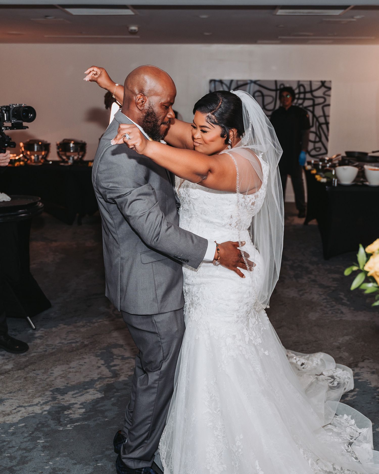 Wedding couple dancing together at their reception, with bride in white dress and groom in grey suit.