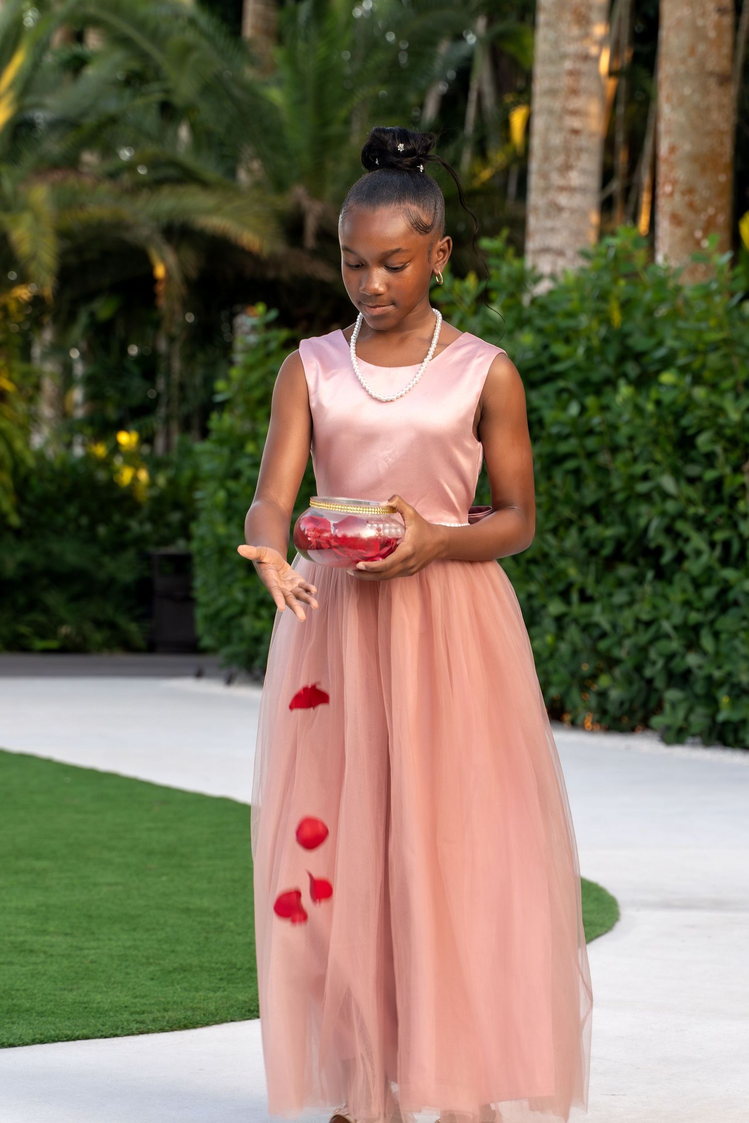 Young flower girl in a peach dress scatters red rose petals along a white aisle runner.