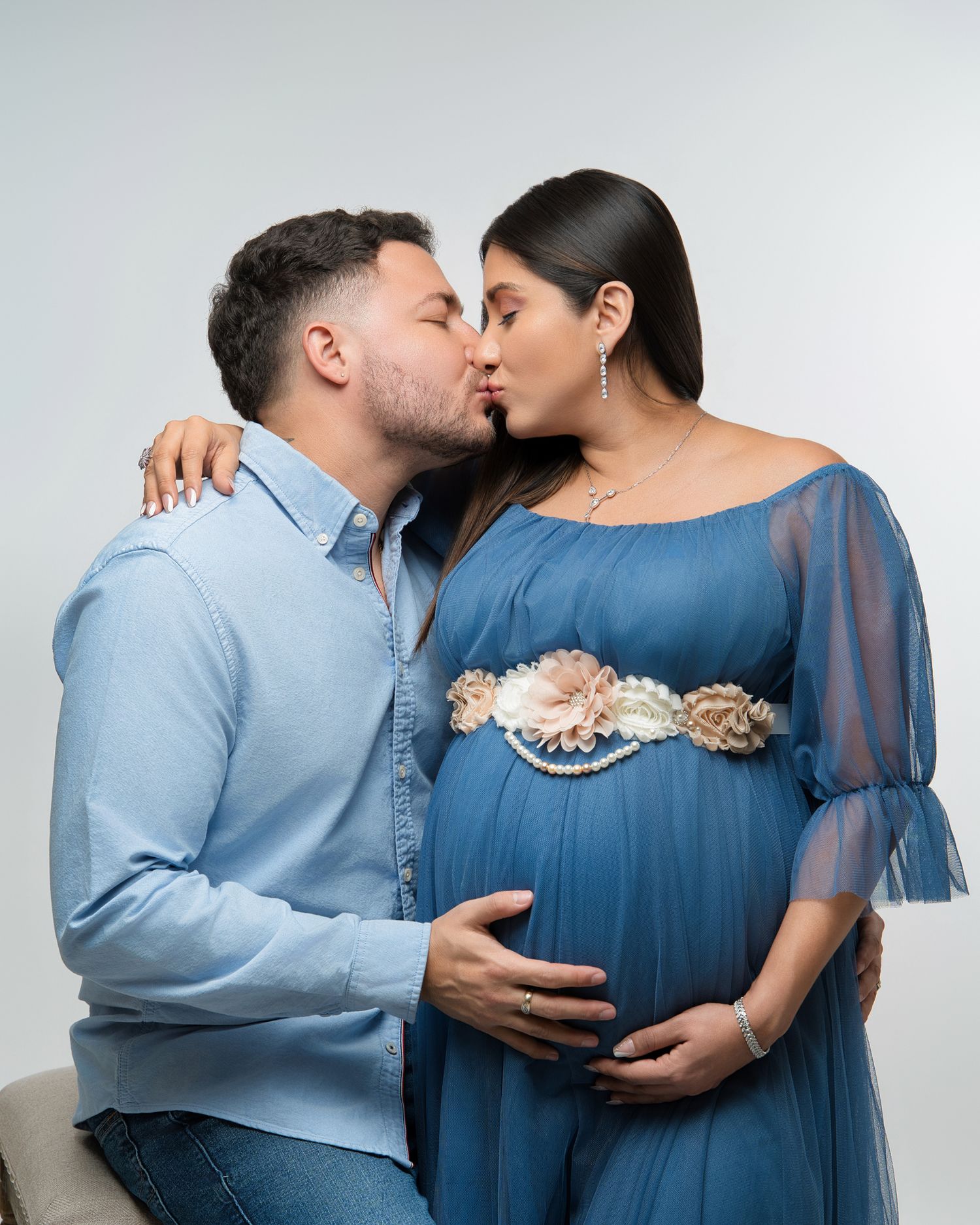 An intimate maternity photo shows a couple sharing a tender moment in matching blue attire.