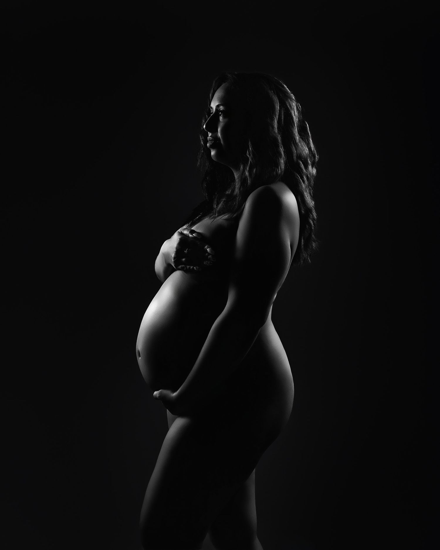 Dramatic black and white silhouette of pregnant figure in profile.
