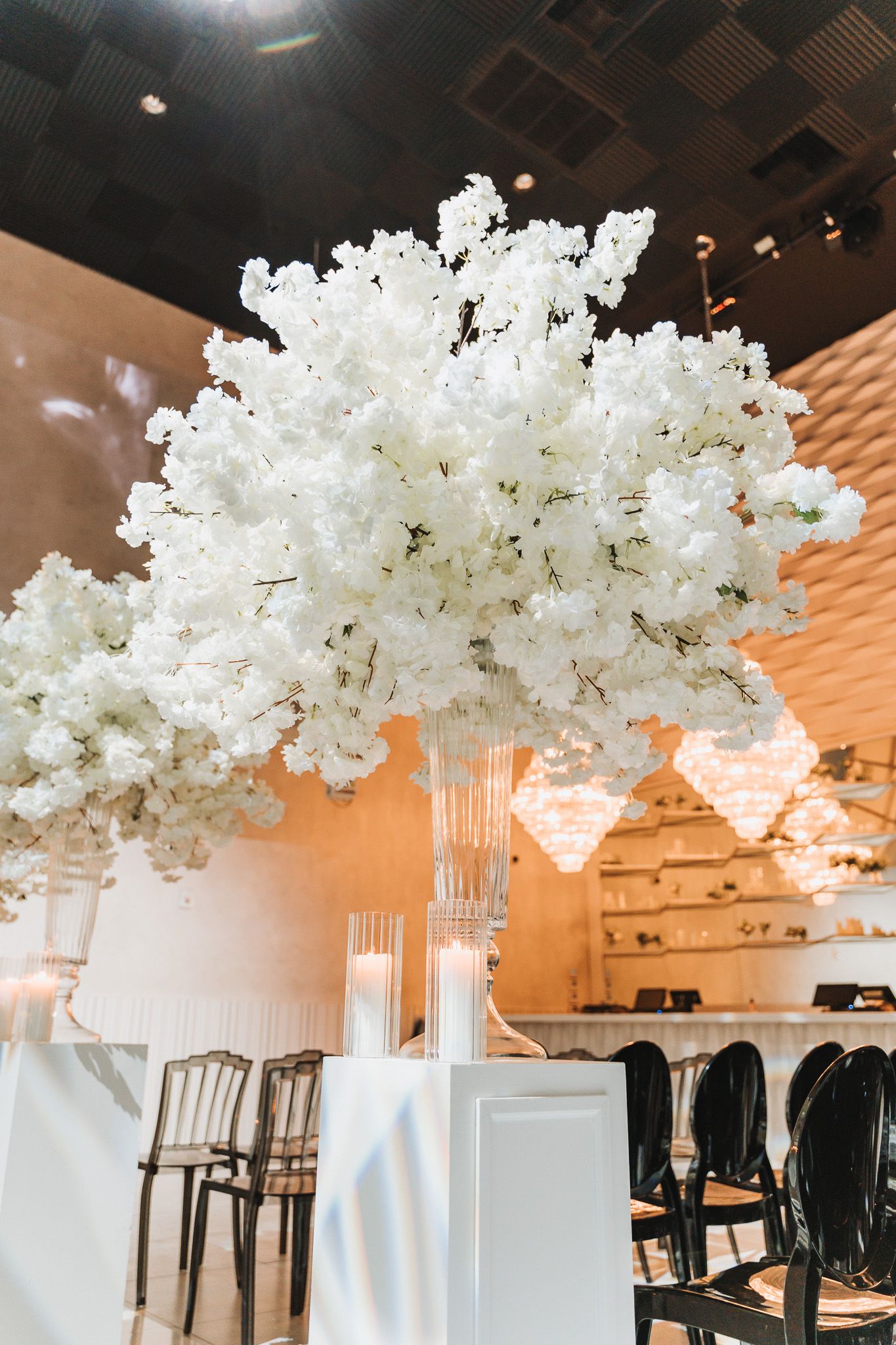 Dramatic white cherry blossom arrangement in tall glass vase at an elegant event setting.