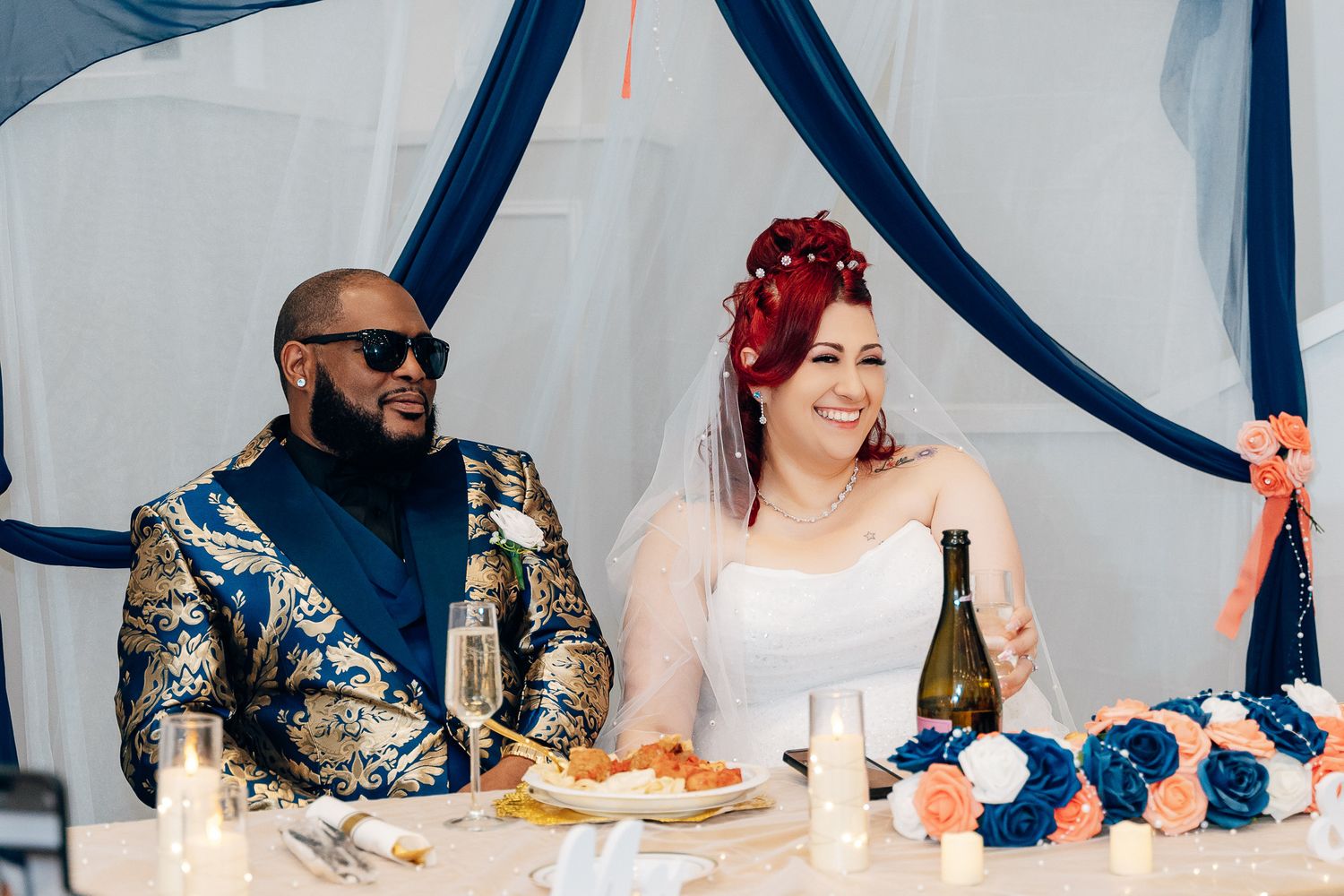 Couple seated at wedding reception head table with navy and white decor.