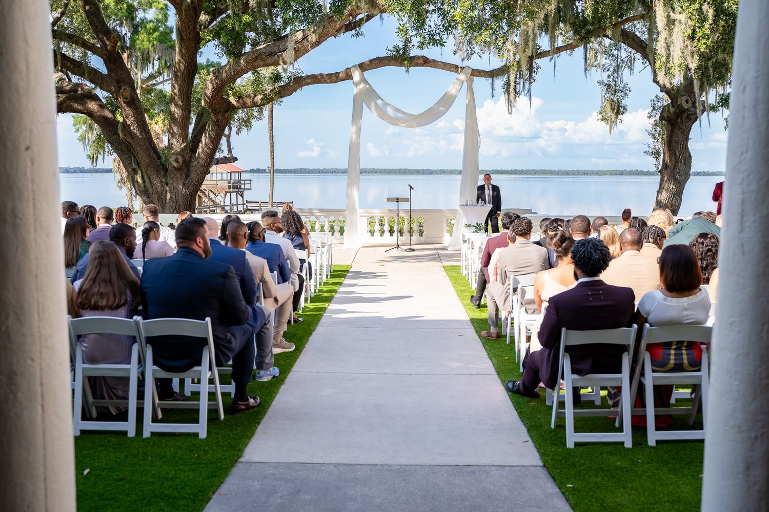 Outdoor wedding ceremony setup with white aisle runner and chairs under oak trees.