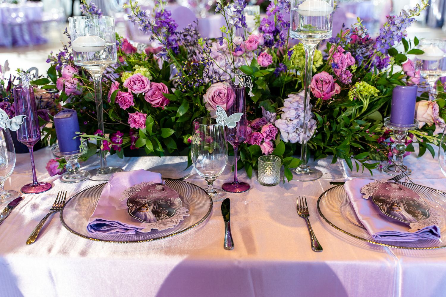 Elegant table setting with purple and pink floral centerpieces and formal place settings.