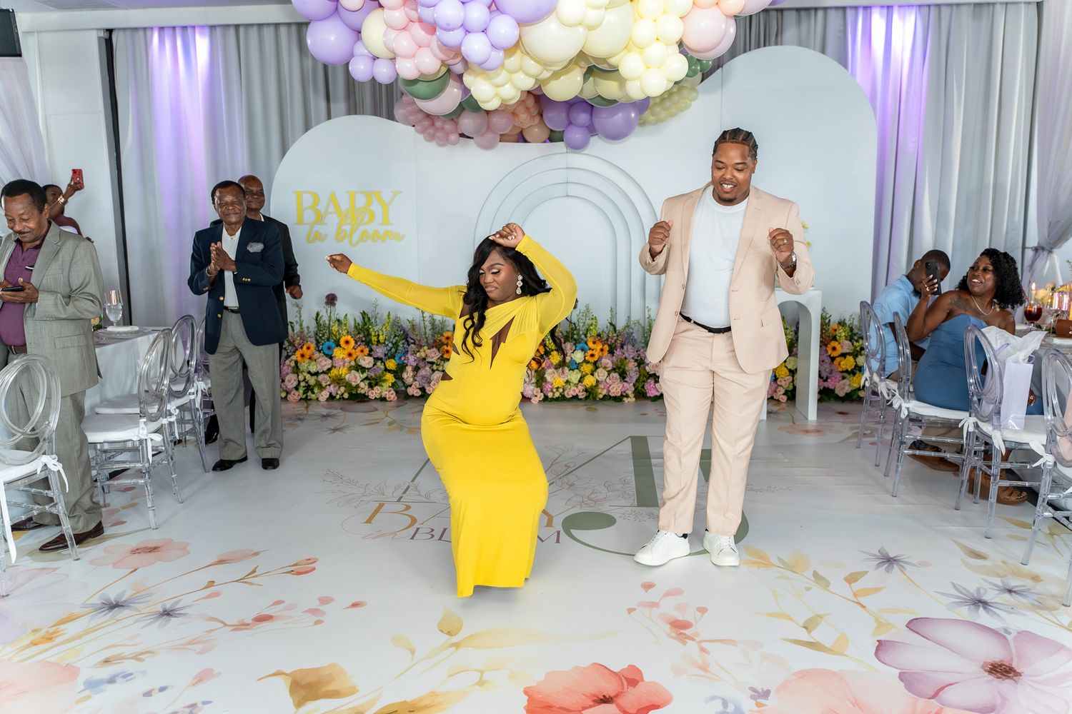 Two guests dancing energetically at a celebration with balloon and floral decorations.