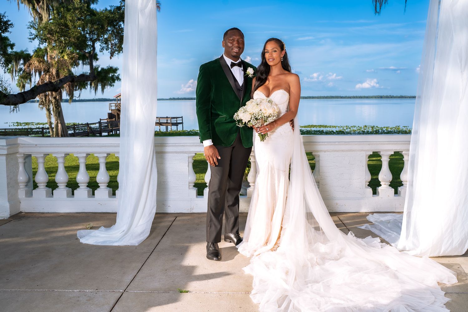 Newlyweds pose for formal portrait at waterfront venue with white columns and flowing wedding dress.