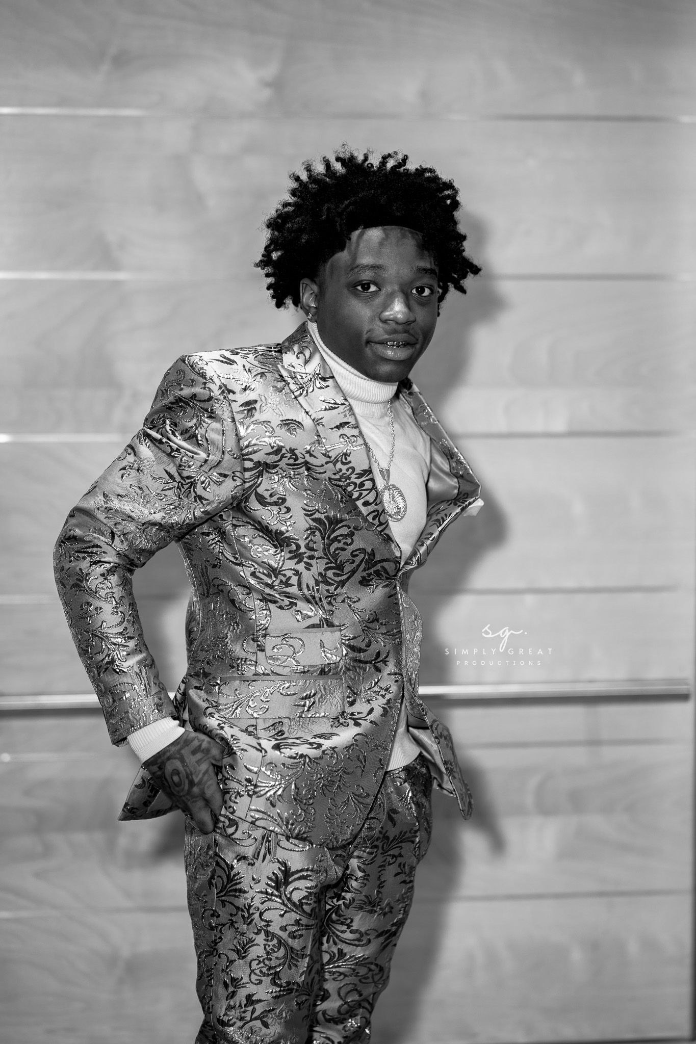 Black and white photo of someone posing in a silver patterned suit.