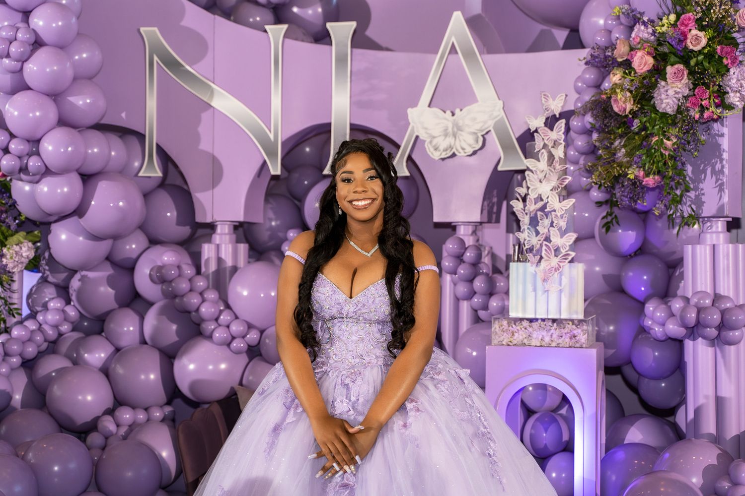 A purple and white themed quinceanera celebration with balloon decorations and floral arrangements in an elegant venue.