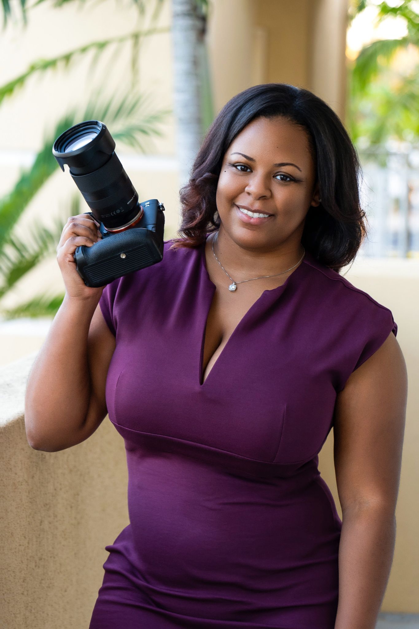 Professional photographer in purple dress holding camera outdoors.