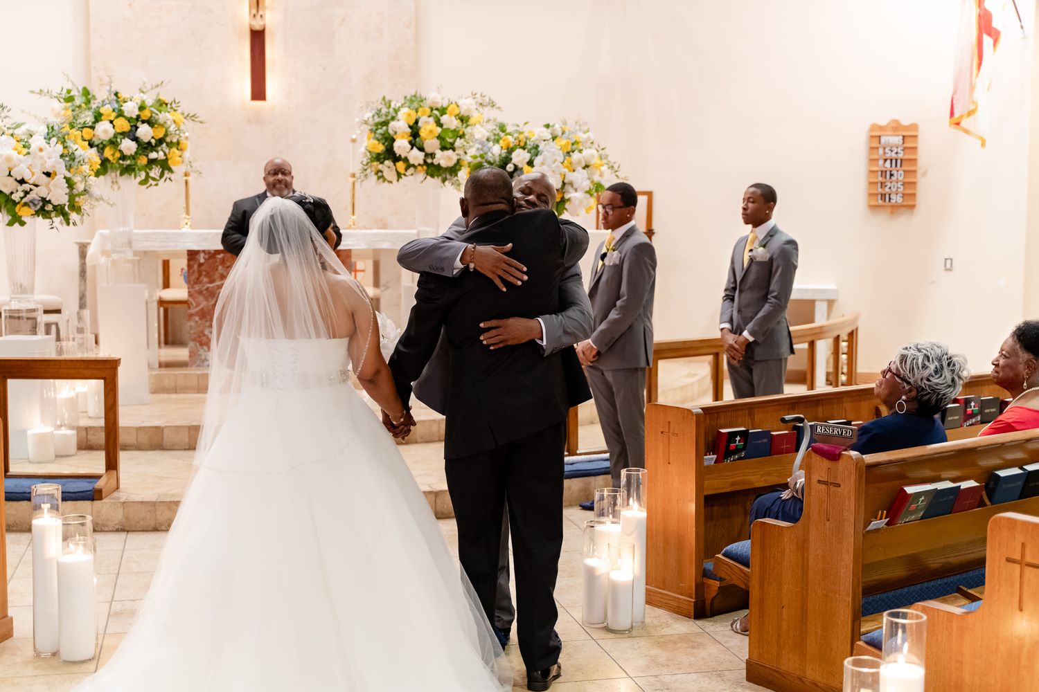 Bride in white wedding dress walks down church aisle with attendant during ceremony.