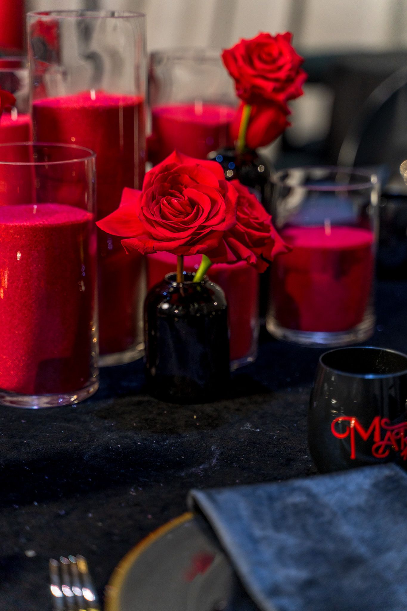 Red roses in black vases with glowing red candles on an elegant table setting.