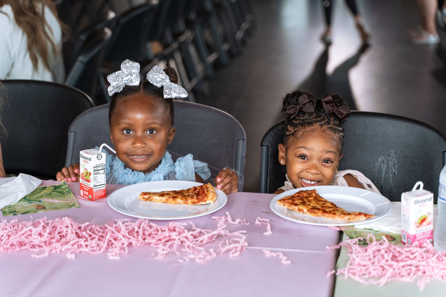 Two children enjoying pizza and refreshments at pink decorated party table.