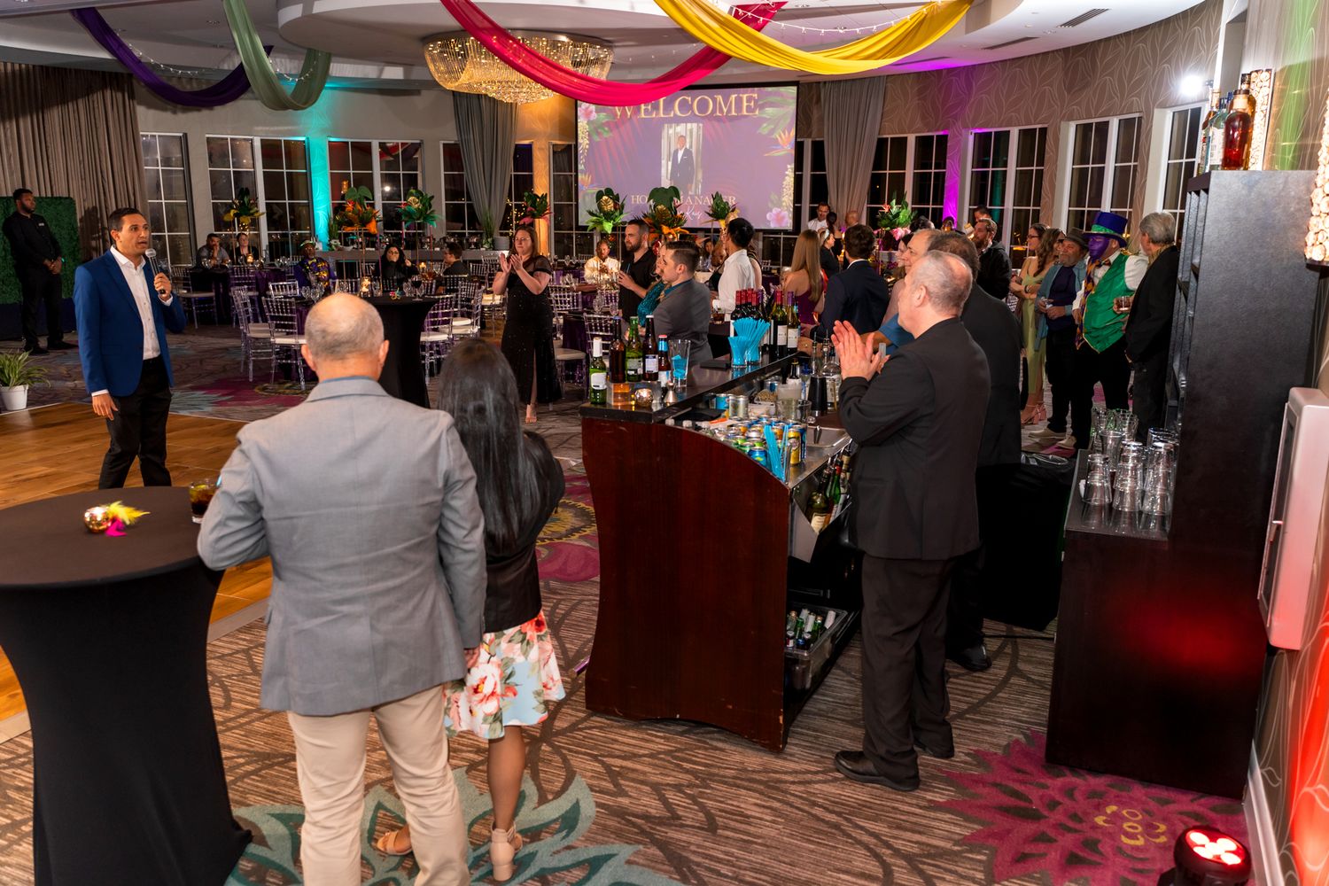 Guests mingling at a corporate event in a banquet hall with colorful ceiling decorations.