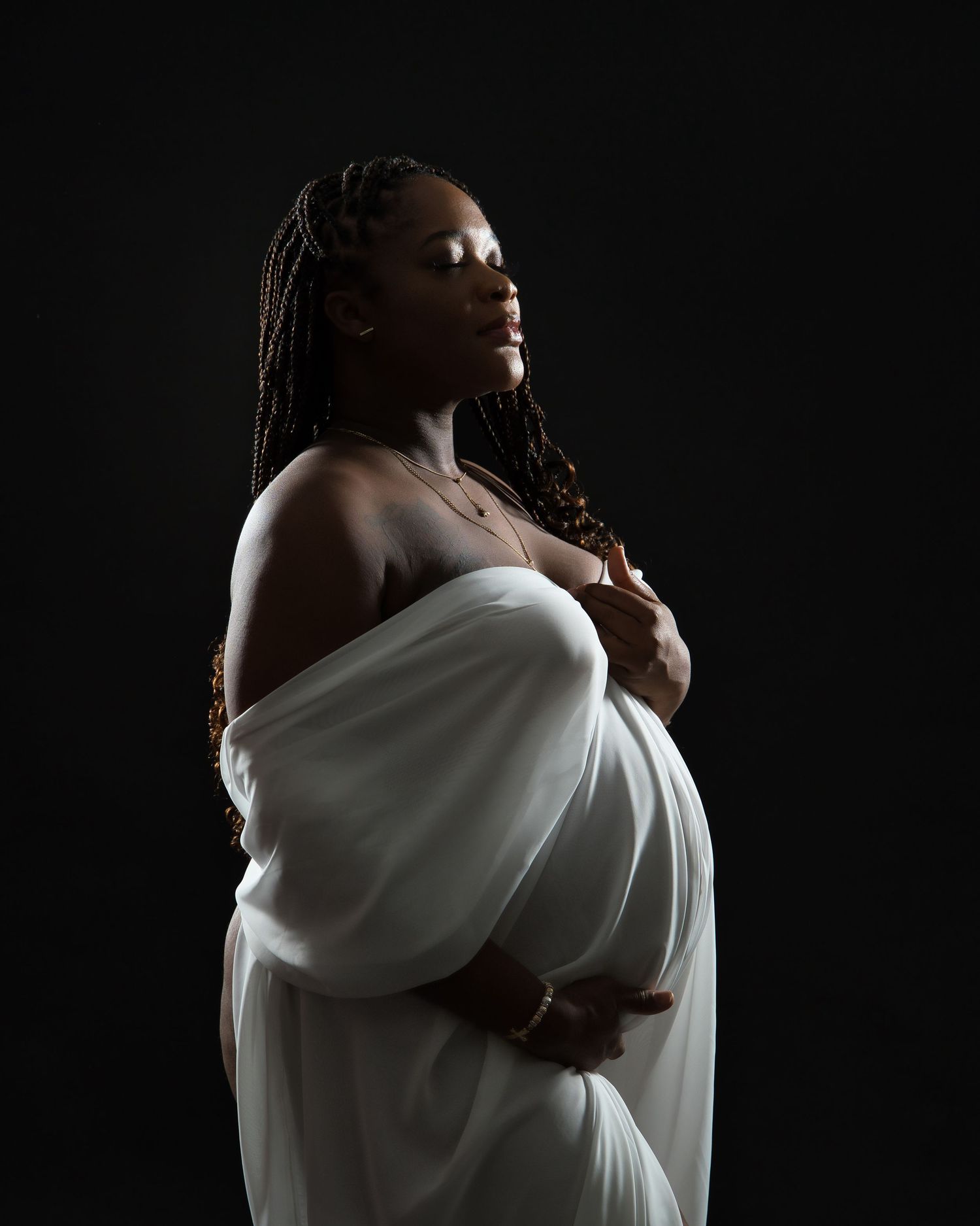 An artistic black and white maternity portrait captures an expectant mother draped in white fabric.