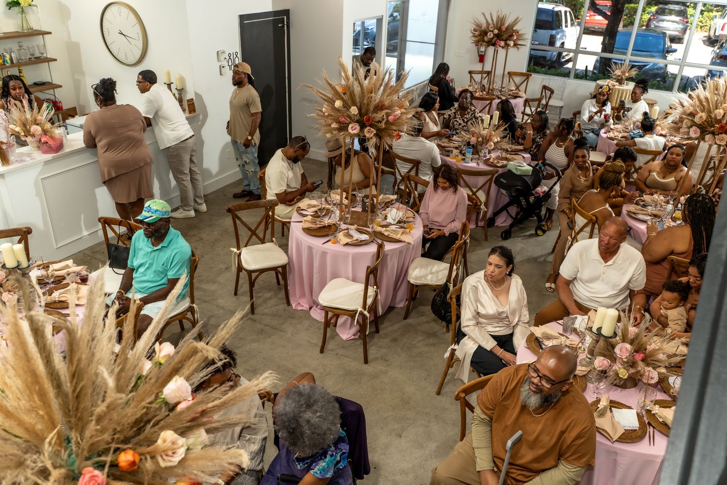 Wide view of celebration space with guests seated at round tables with neutral and pink decor.