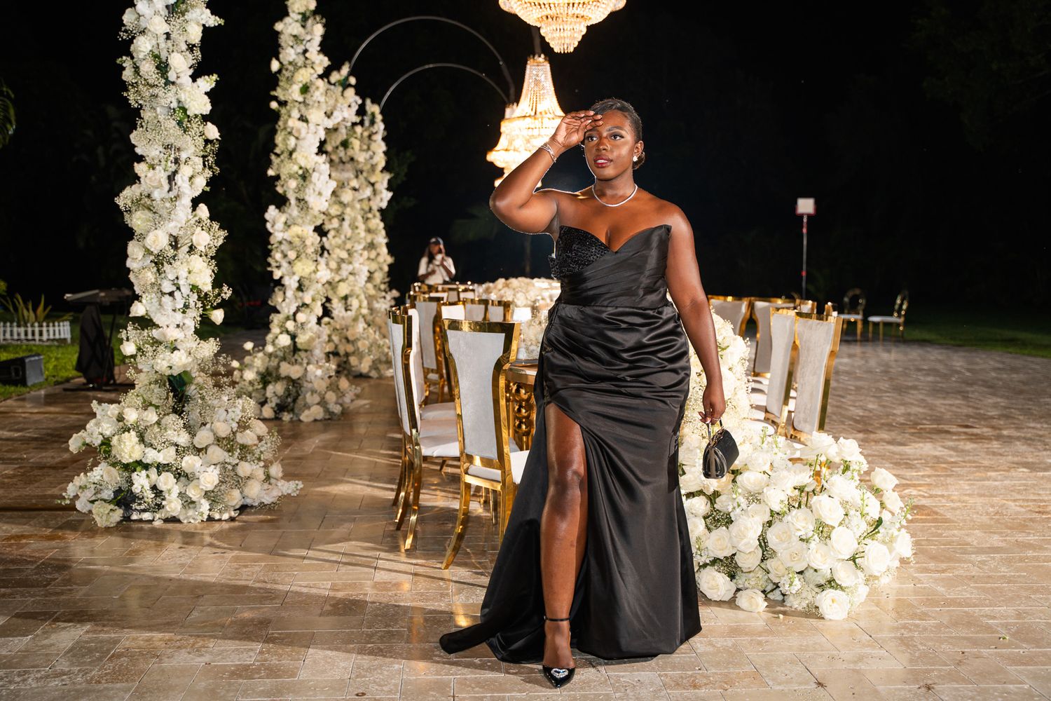A formal evening celebration setup with white floral arches and elegant gold chairs against a dark backdrop.