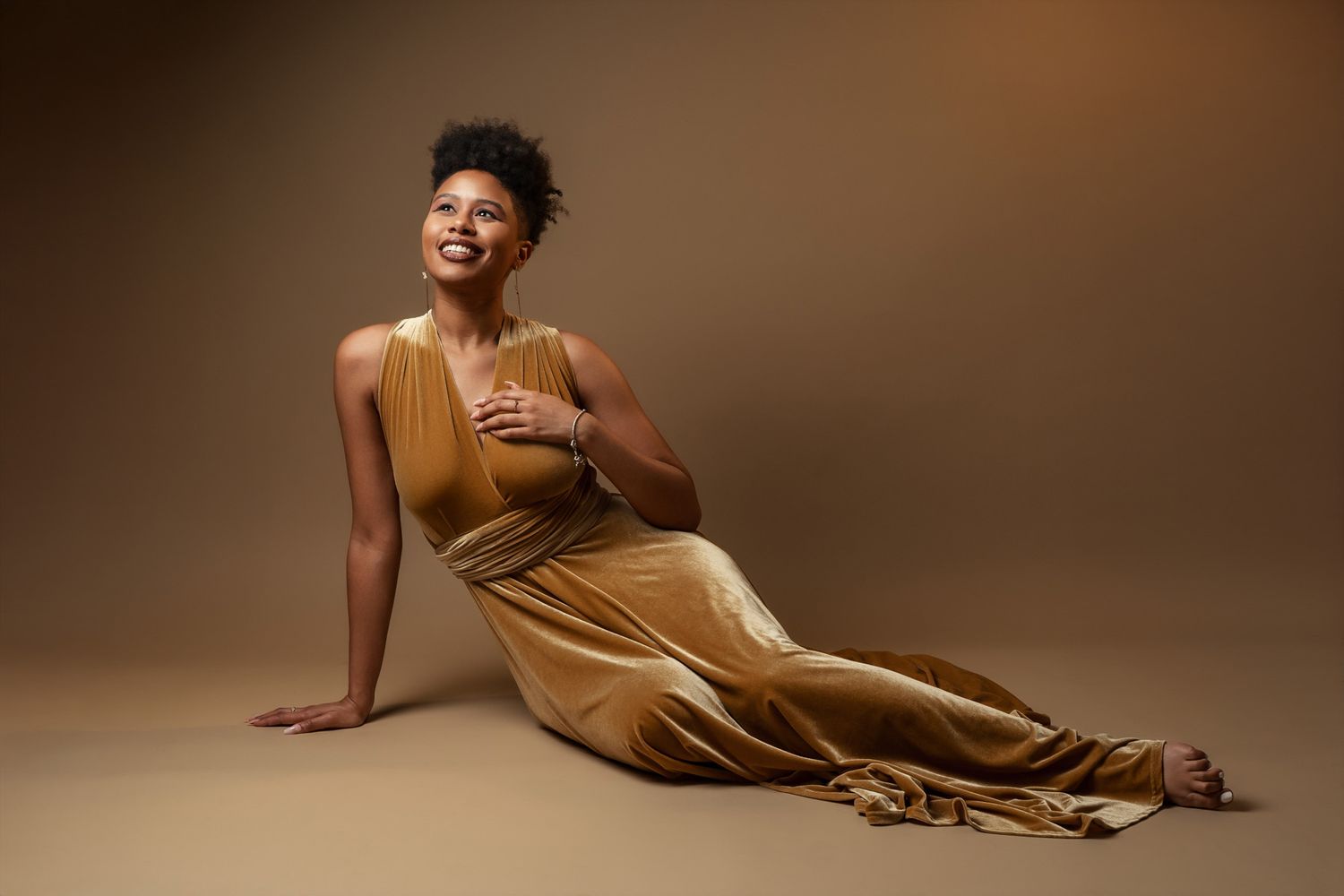 Woman in gold dress poses gracefully on floor during studio photoshoot.