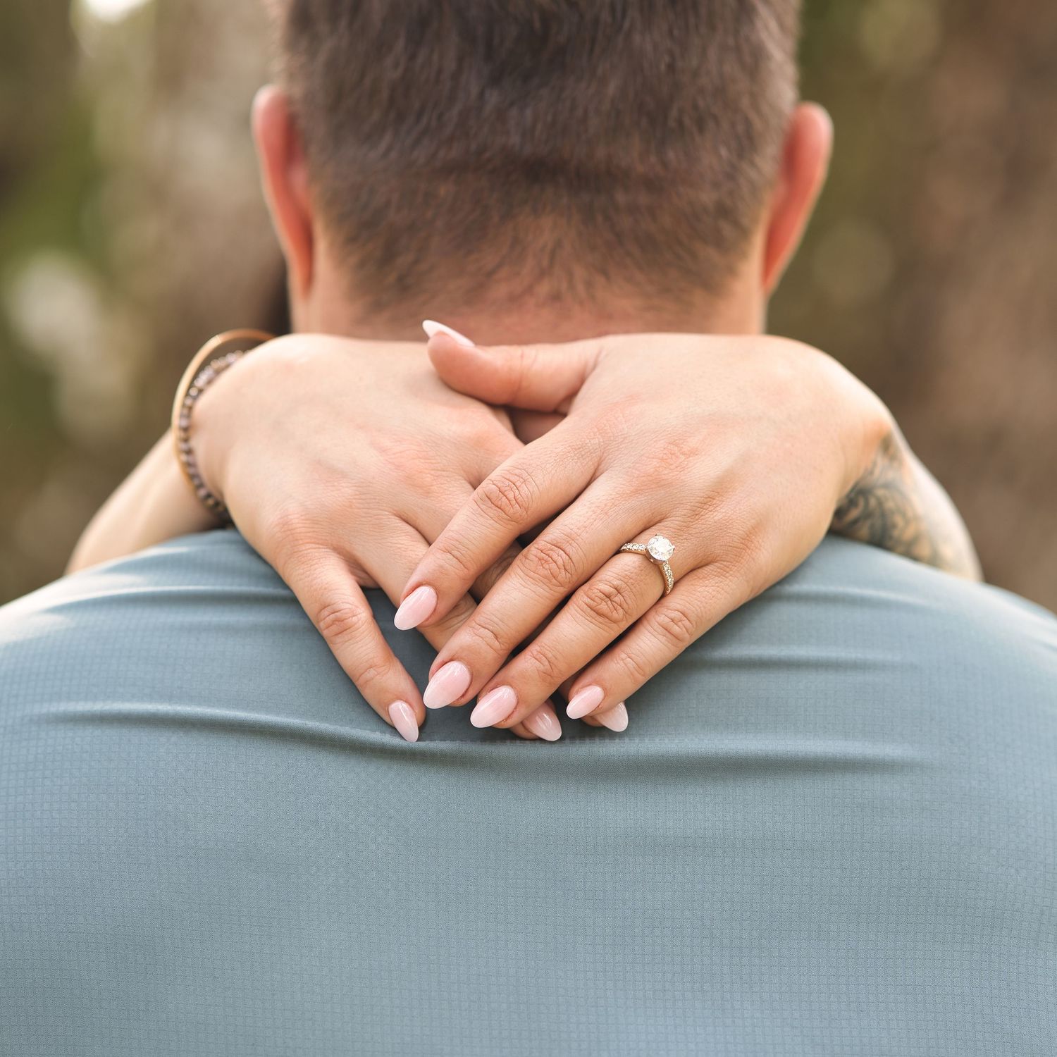 Hands with engagement rings embracing in a romantic moment against a blue shirt.