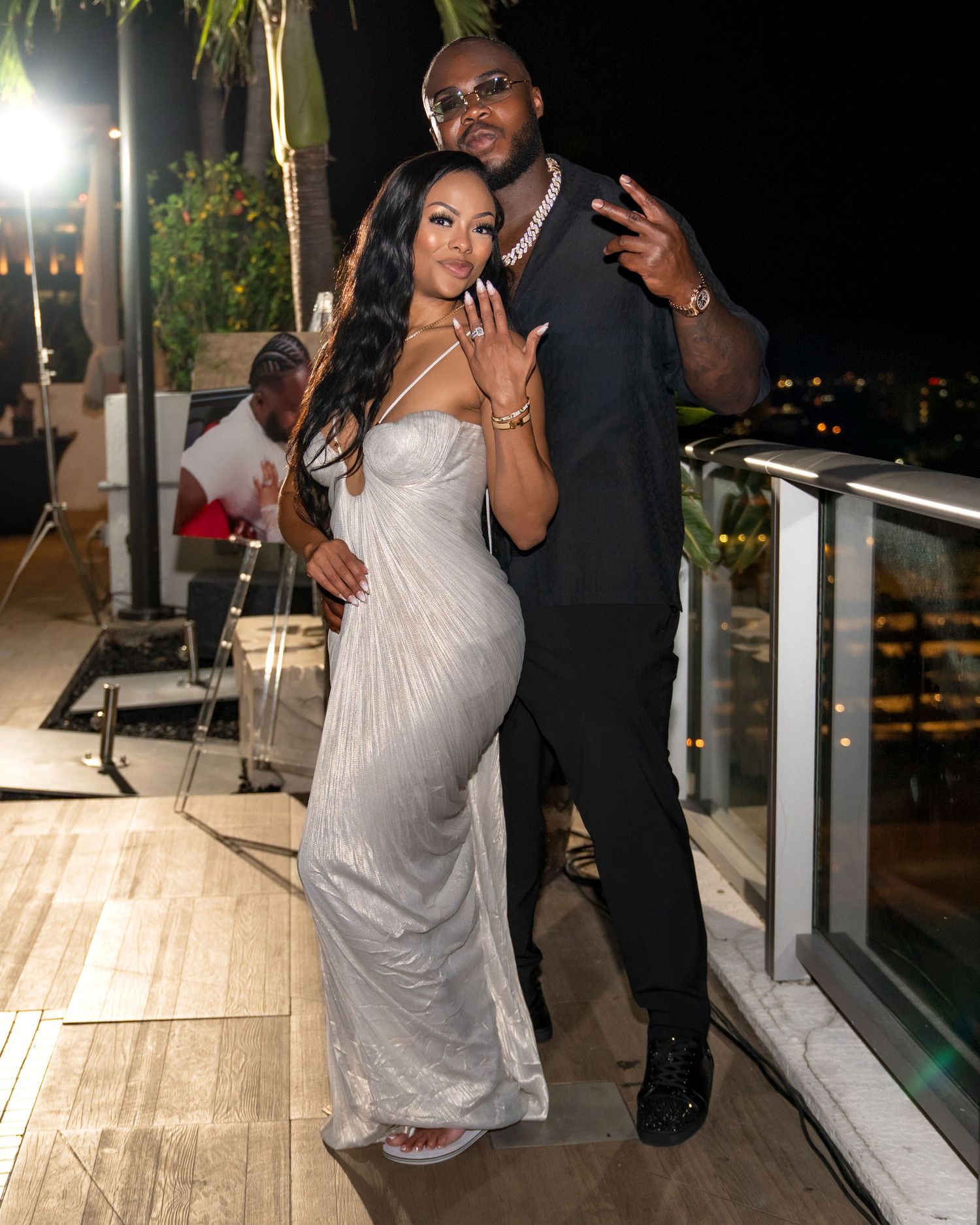 A couple poses together on an outdoor deck at night, with the woman wearing a silver evening gown.