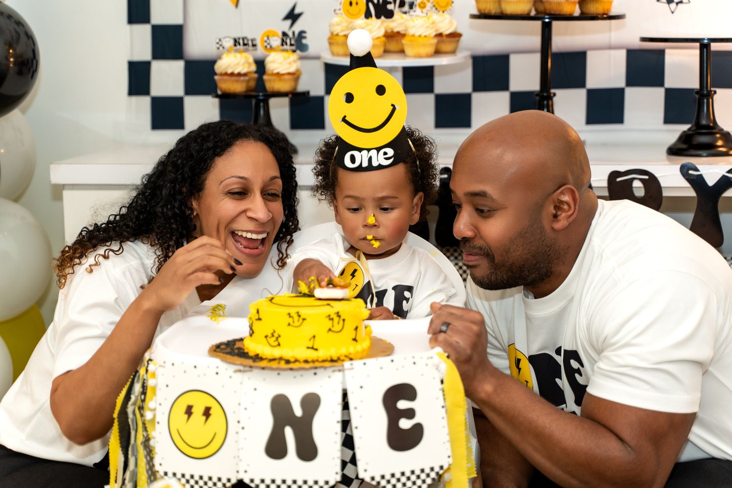 A smiley face themed first birthday celebration with a round cake and yellow decorations.