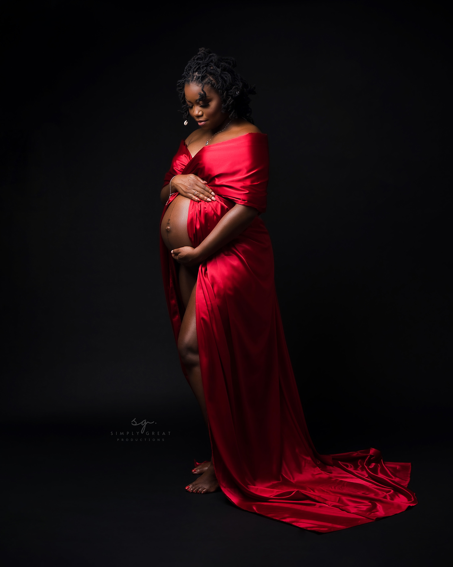 Artistic maternity portrait with flowing red dress against dramatic black background.