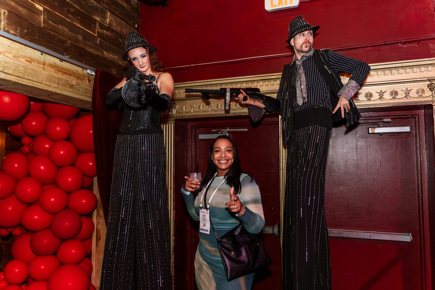 Entertainment performers in black striped costumes posing against red balloon wall.