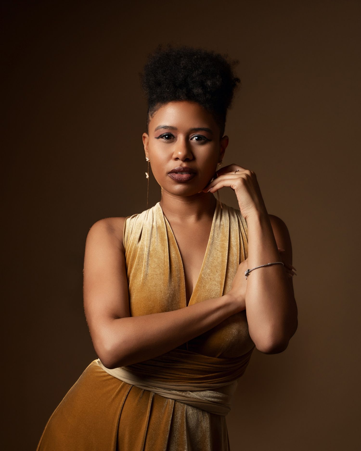 Portrait of woman in gold dress against brown background with dramatic studio lighting.
