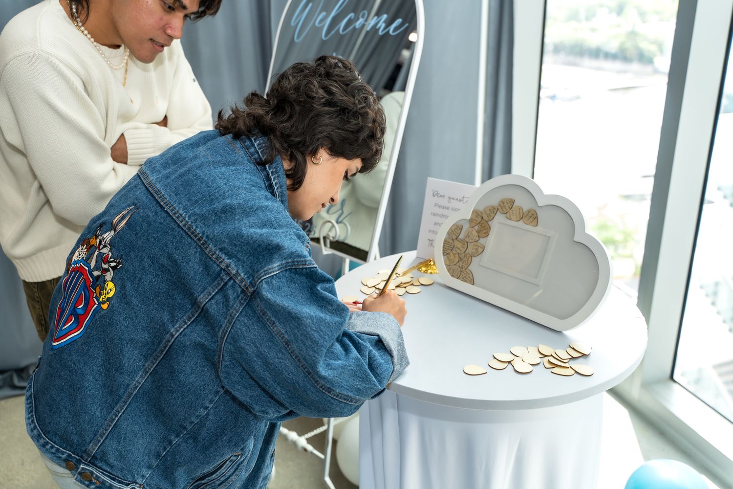 Guest signing a decorative guest book at an event near window.