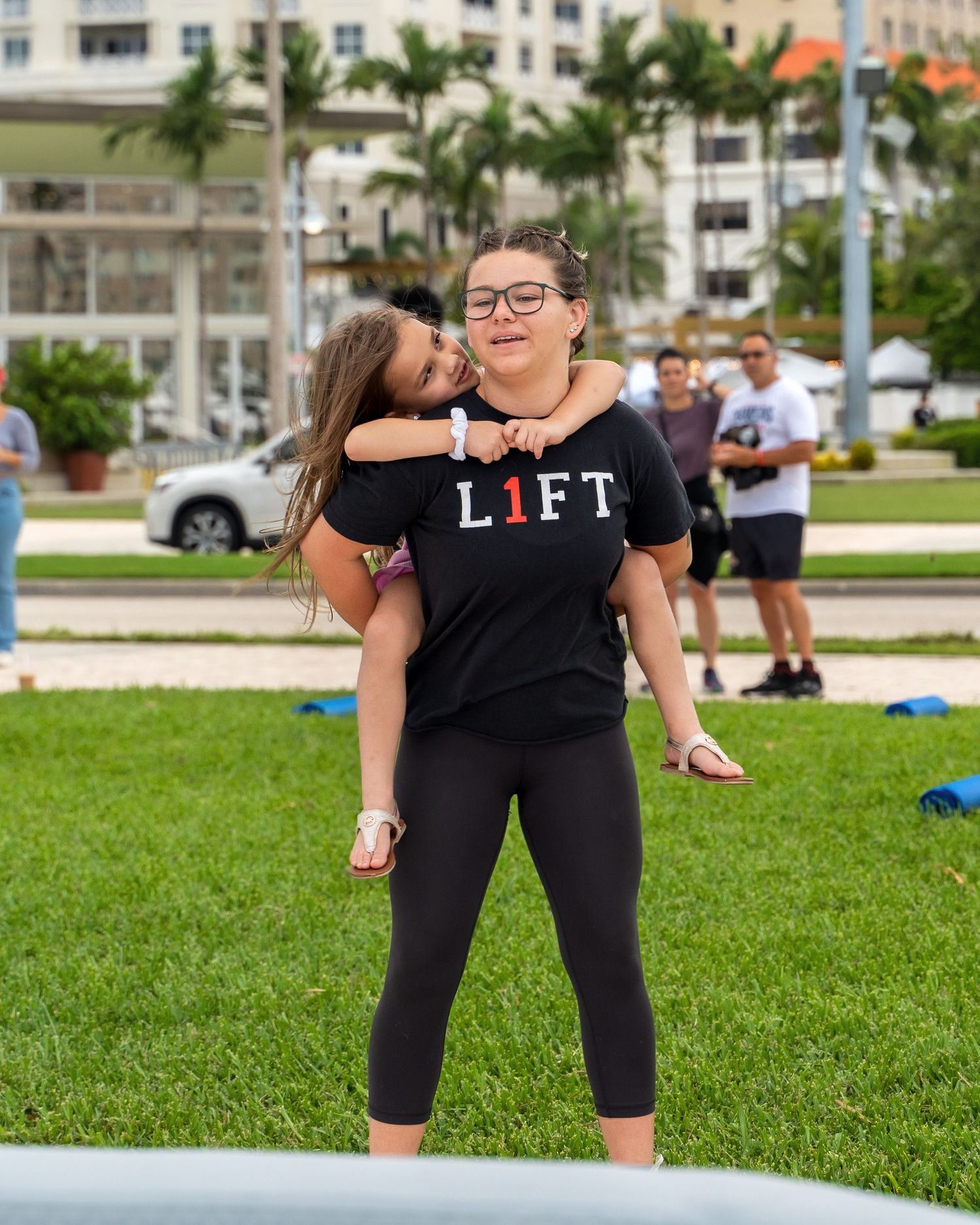 People engaging in outdoor fitness activities on a grassy area with palm trees and buildings in background.