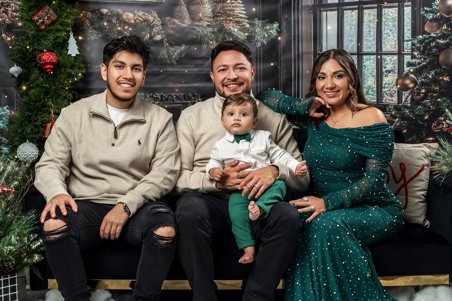 Holiday family photo featuring festive Christmas backdrop, emerald green dress, and coordinated outfits.