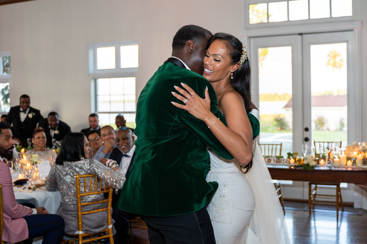 Wedding couple embraces during first dance with groom in emerald velvet jacket.