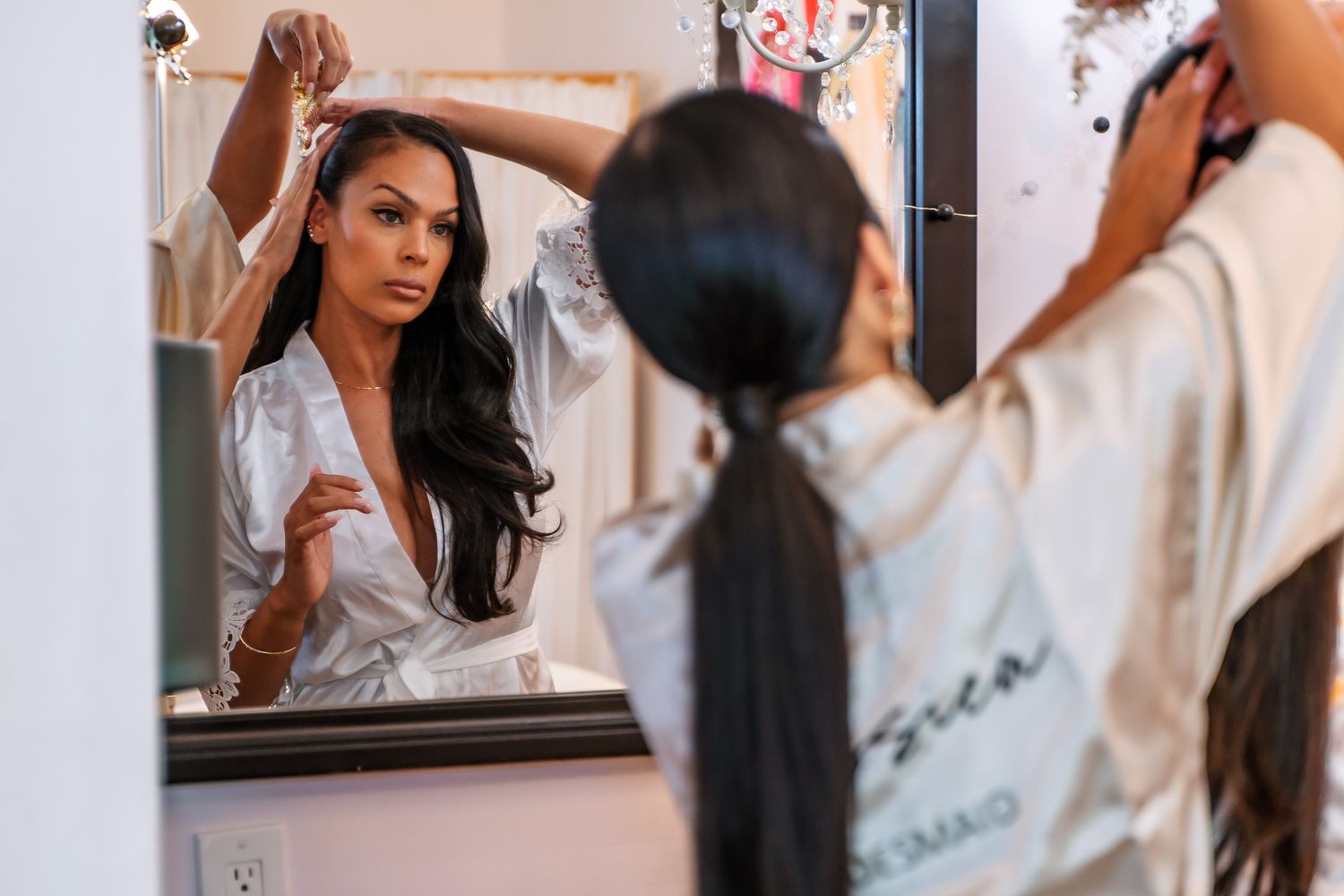 Someone applying makeup in a bathroom mirror while wearing a white silk robe.