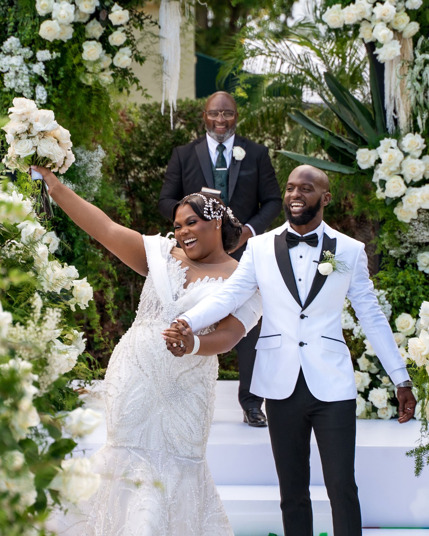 Newlyweds celebrate joyfully during their outdoor wedding ceremony surrounded by white floral decorations.