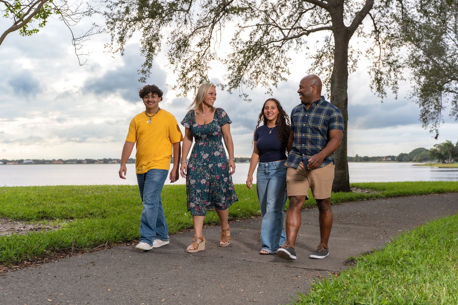 People walking together on a grassy path near a waterfront on a cloudy day.