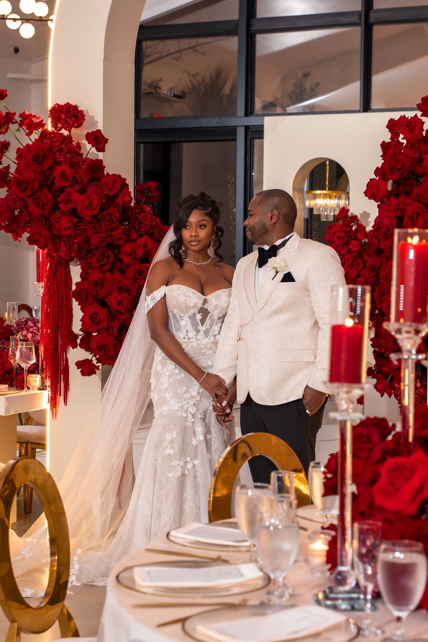 Elegant wedding reception table decorated with towering red rose centerpieces and gold accents.
