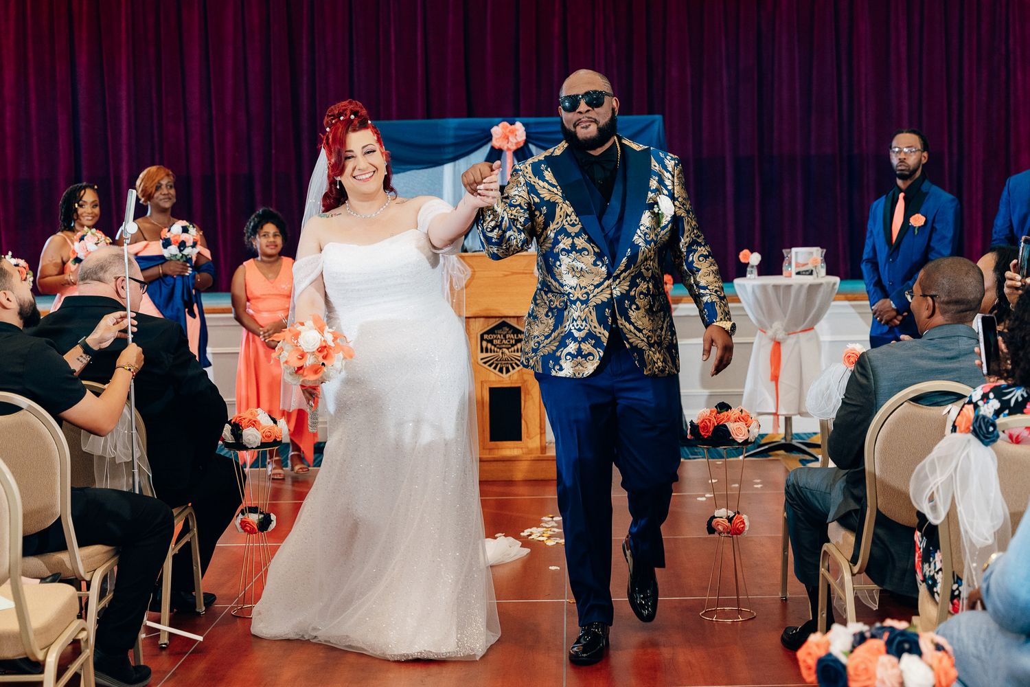Wedding couple walking down aisle together as guests look on.