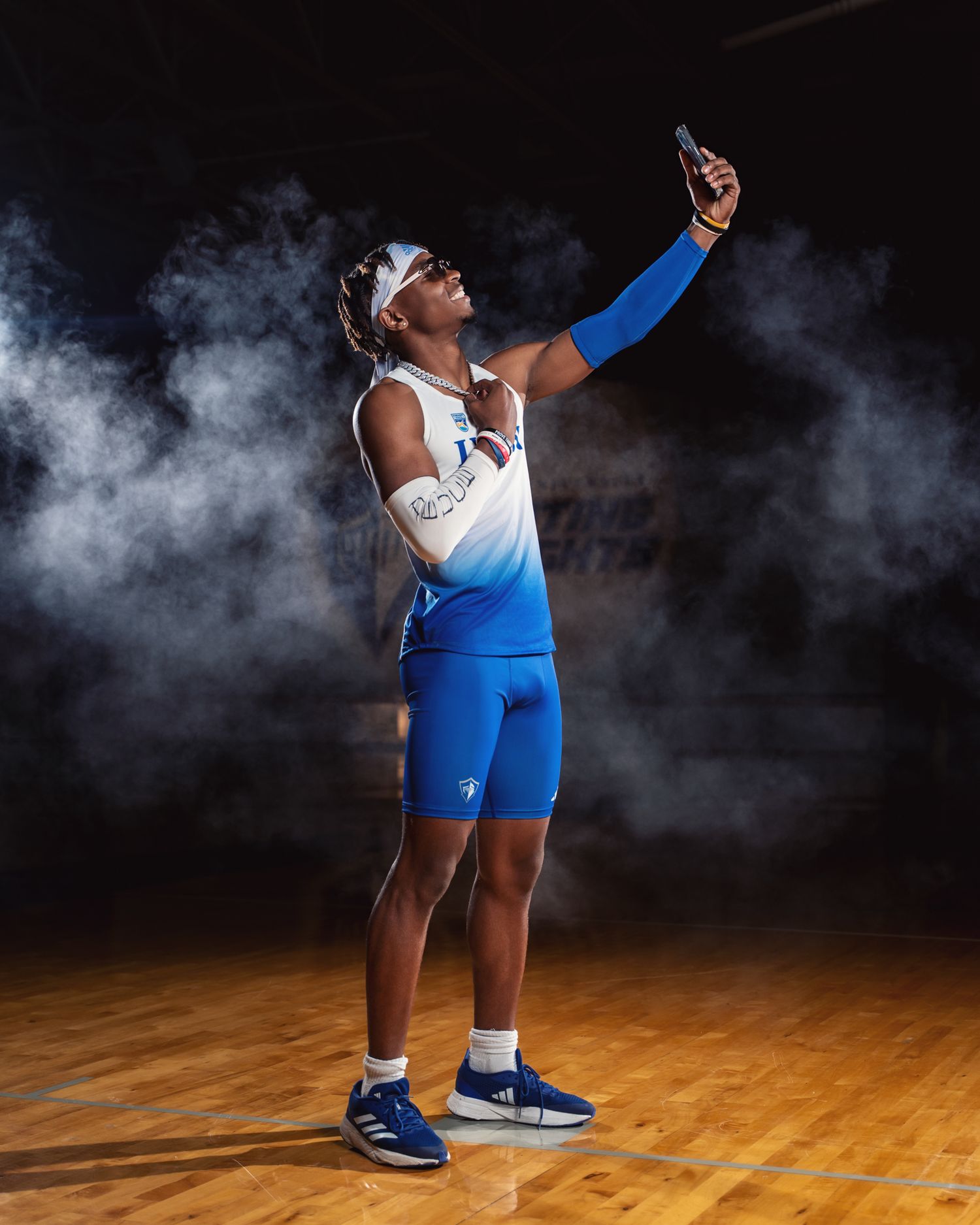 Lynn athlete poses dramatically with raised arm amid smoke effects on wooden court.