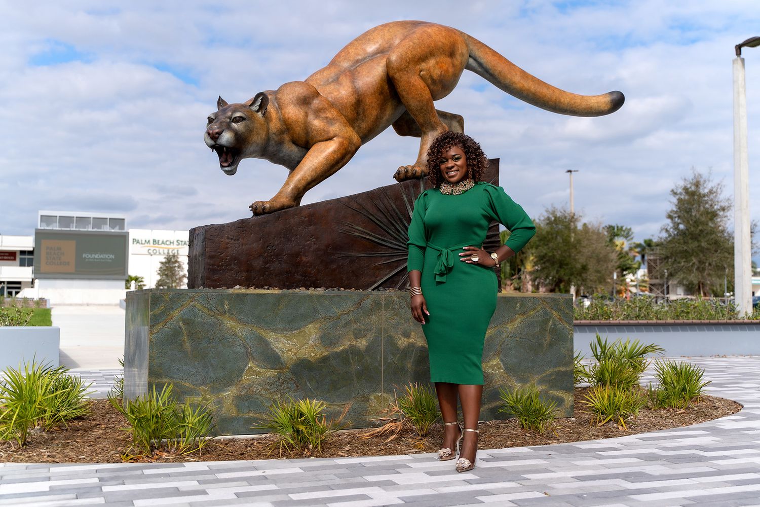 A green dress-clad figure poses in front of a large bronze mountain lion statue on a stone pedestal.